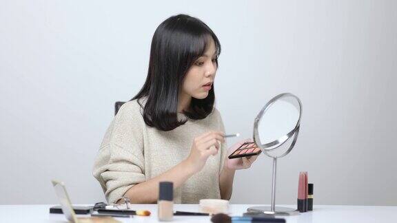 年轻的亚洲女性用刷子在眼睛周围涂抹眼影美丽的女人看着镜子和化妆