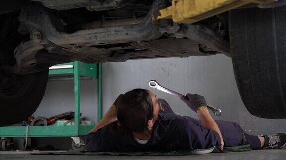汽车修理工躺在车下检查用扳手和手电筒修理汽车修理厂汽车修理工工作