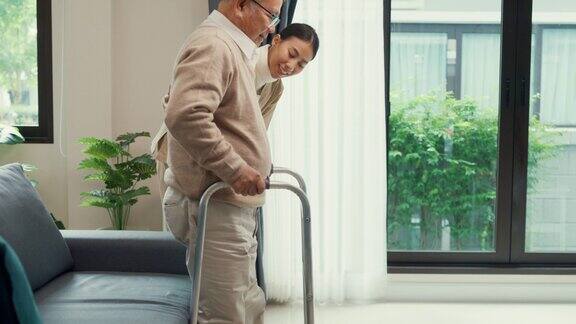 年轻的亚洲女性护理人员教老男性走路使用助行器照顾在家里的客厅握着老人的手