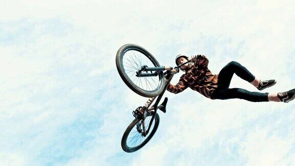 年轻男子在多云的天空下跳跃和旋转BMX自行车