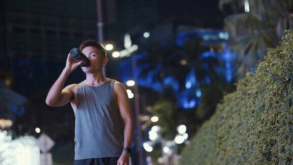 晚上下班后一名亚裔中国男子在城市慢跑后喝水