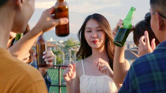 一群年轻的亚洲人在日落时分和朋友们一起享受拿着啤酒瓶在屋顶派对上跳舞