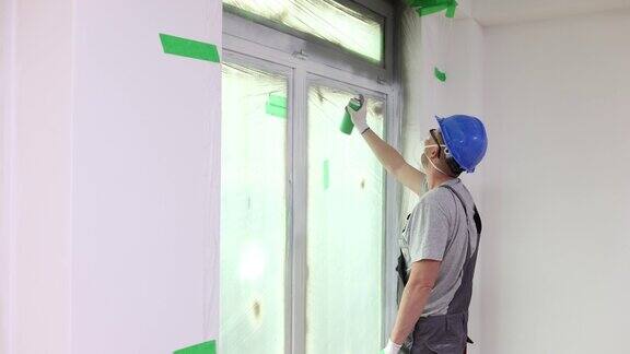 戴头盔的建筑工人在窗框上喷灰漆