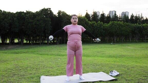 年轻高大的亚洲女性在户外用哑铃锻炼