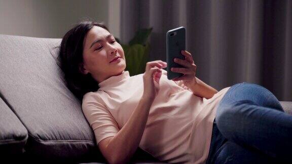 亚洲妇女坐在沙发上拿着智能手机在家