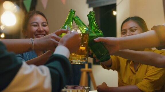 一群多民族年轻的亚洲朋友喝着酒啤酒瓶玻璃有乐趣的笑声享受聚会的夜生活在室内的家