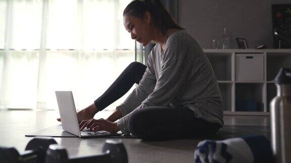 运动的亚洲年轻女性在家锻炼在互联网上观看健身视频或在线健身课程使用笔记本电脑客厅室内