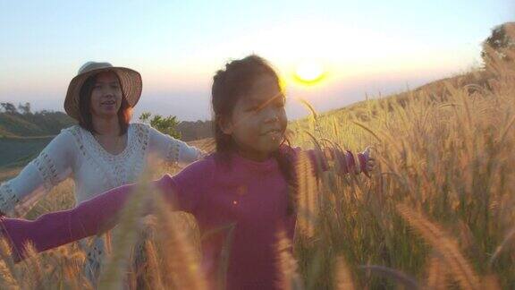 亚洲女孩和母亲在日落时分穿过草地