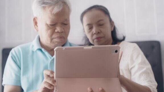 周末度假时亚洲的老夫妇在家里的卧室里用平板电脑阅读社交媒体老年人幸福生活
