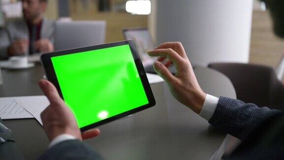同事在商务会议桌上滚动平板电脑绿屏浏览网页