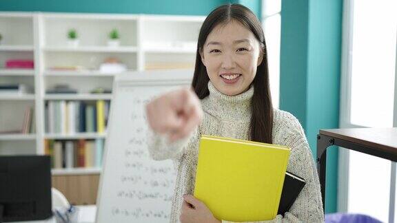 在图书馆大学年轻的中国女学生拿着书用手指着相机