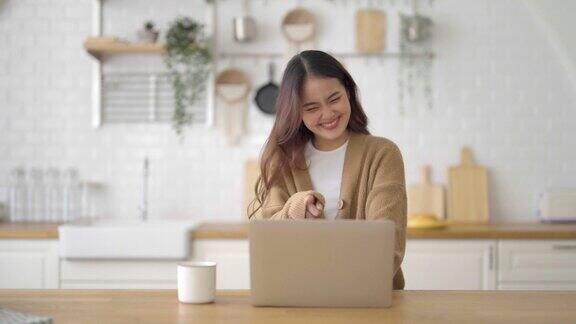 微笑的亚洲年轻女性在家里的笔记本电脑上工作年轻的亚洲学生使用计算机远程学习虚拟培训电子学习观看在线教育在家里的网络研讨会