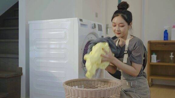 快乐的年轻亚洲妇女从洗衣机里取出干净的衣服把衣服放进篮子里疲惫的家庭主妇在工作