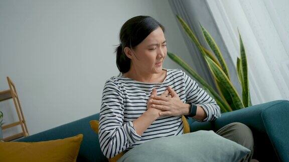 一位亚洲妇女坐在家里客厅的沙发上感到胸痛