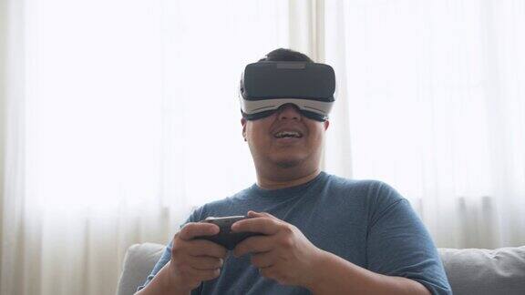 快乐的亚洲人坐在沙发上戴着VR虚拟现实眼镜玩在线视频游戏