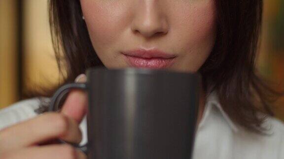 女性在室内喝热茶的详细微镜头慢镜头不认识的女人拿着一杯咖啡与化妆近距离没有脸嘴唇、口红、面部美容化妆品