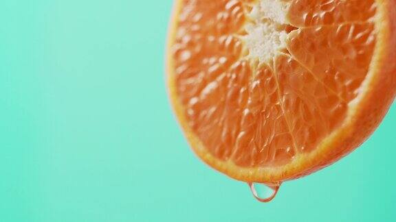 在绿松石色的背景上一滴果汁从美丽多汁的橘子边缘落下特写富含维生素C的健康柑橘类水果