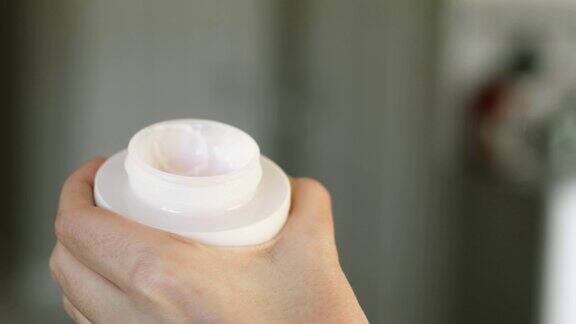 女人正在打开一个白色的塑料罐子用奶油特写的手