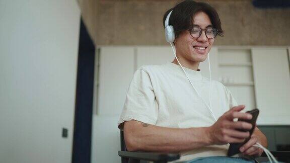 微笑的亚洲男子在家里打字听音乐