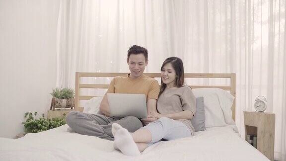 亚洲夫妇躺在床上休息时使用笔记本电脑夫妇在家里玩电脑社交媒体夫妇使用在家放松时间