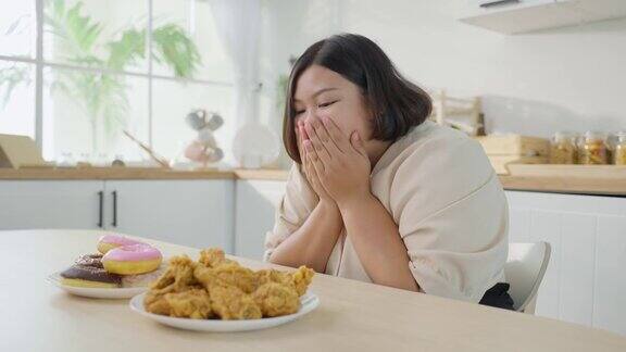 亚洲年轻的胖女人为盘子里的不健康食物感到高兴诱人的美丽的加码女孩感到饥饿准备吃炸鸡和甜甜甜圈在家里的餐桌上