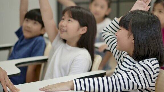 一群快乐的亚洲小学生在课堂上举起手臂回答老师的提问幼儿园学前概念