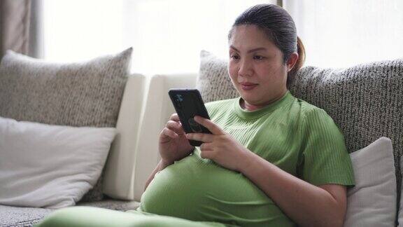 身着绿色套装的孕妇坐在家里客厅的沙发上使用手机