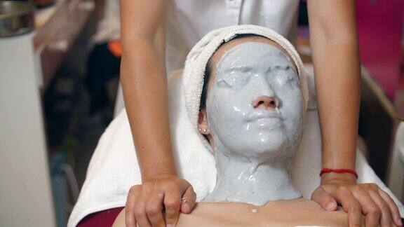 年轻的亚洲女性在水疗中心使用维生素面膜和肩部按摩