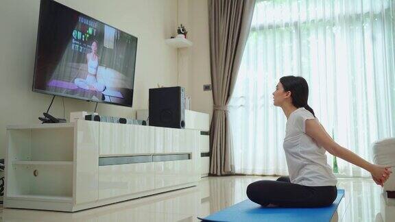 亚洲美丽的年轻女子呆在家里按照在线教练的指导视频锻炼活跃的女孩在室内做封锁活动在冠状病毒大流行期间做瑜伽普拉提锻炼