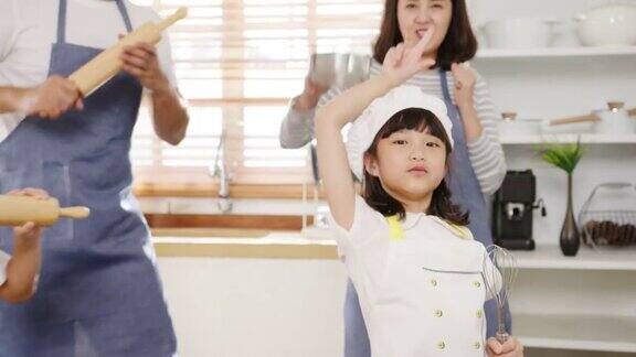 快乐的年轻亚洲家庭和学龄前的孩子们在厨房里做早餐一边听音乐一边跳舞
