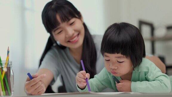 快乐的亚洲男孩与他的母亲在客厅里用蜡笔和彩色铅笔画画妈妈教儿子如何用蜡笔在书上画画或做作业家庭