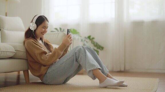 快乐的年轻亚洲女人在家里放松女性微笑着坐在沙发上手里拿着手机女孩用视频打电话给朋友