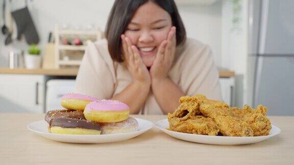 亚洲年轻的胖女人为盘子里的不健康食物感到高兴诱人的美丽的加码女孩感到饥饿准备吃炸鸡和甜甜甜圈在家里的餐桌上