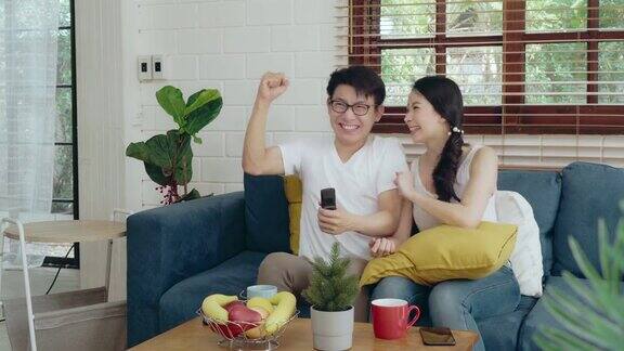 两个年轻的亚洲夫妇家庭在沙发上放松看电视cheerup足球比赛亚洲的生活方式在家