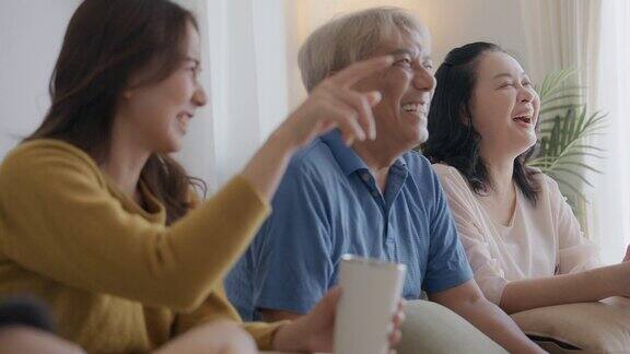 一位老人带着女儿和孙女坐在家里的沙发上看电视笑得很开心