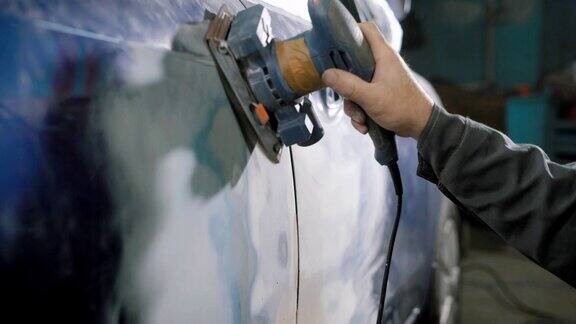 在汽车车间里工人正在用手工打磨机清除车身上的旧蓝色染料为喷漆做准备