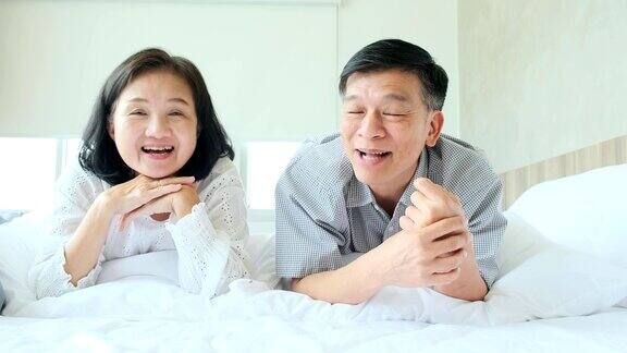 幸福安康健康的老亚洲夫妇笑着一起笑着享受躺下休闲在床上快乐的老夫妇躺在床上看垫相机慢镜头