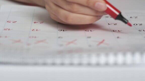 日历页面模糊特写女性手划掉日历上的日子用钢笔在日历上标出的红圈