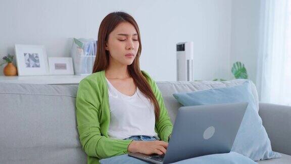 精疲力尽的亚洲女商人伤害眼睛而使用笔记本电脑年轻的女职员坐在沙发上感觉视觉疲劳和眼睛疲劳劳累和按摩干燥易怒的眼睛在家