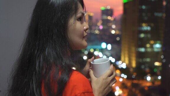 亚洲年轻女子站在阳台上看日落在城市