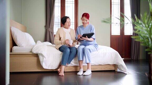 穿着手术服的亚洲女护士报告卧室里有药片的亚洲老年妇女的健康状况看护者上门探访家庭保健和养老院