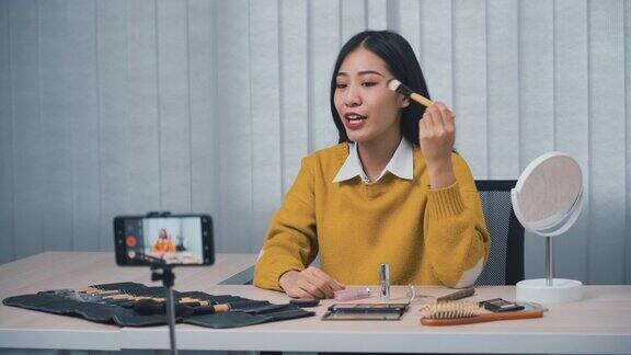 一位年轻的亚洲女性在家里用手机相机拍摄了一段关于化妆品的视频并在她的博客上写了关于美容产品的视频