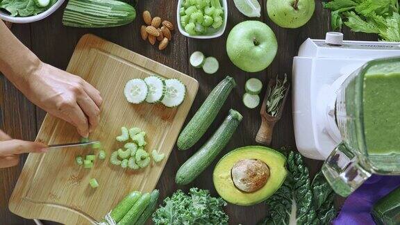 饮食概念:直接向下平移视图拍摄的女人的手切蔬菜排毒奶昔厨房桌上的切菜板和搅拌机