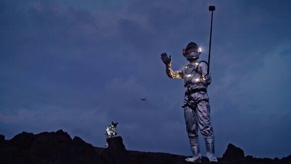 自拍太棒了宇航员穿着未来派的、发光的衣服拿着自拍杆无人机在他们上方飞行