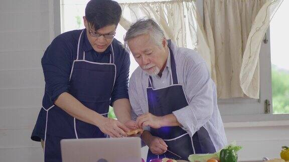 快乐的亚洲年轻人和老父亲享受周末在家准备美味的健康沙拉在家里的厨房