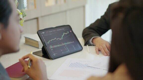 三位财务顾问和交易员坐在一起讨论和监控股票数据在数字平板电脑屏幕上绘制图表显示资金流向集中团队讨论财务规划策略概念