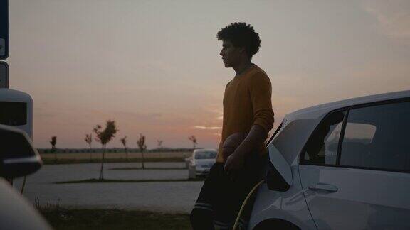 黄昏时分年轻的篮球运动员在停车场给他的电动汽车充电