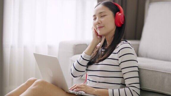 4K年轻的亚洲女子在客厅用笔记本电脑工作时从耳机里听音乐
