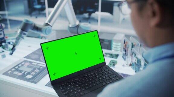 机器人工程师使用绿屏模拟显示屏的笔记本电脑的肩部照片手持微芯片的机械臂自动化创业研发办公室
