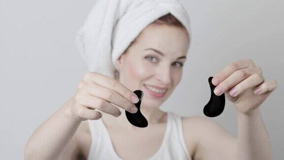年轻女子洗完澡后头上戴着毛巾手里拿着两块黑眼罩